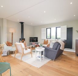 A living room with multiple chairs a sofa a wood burning stove and a TV at Holm Oaks Cottage in Busbridge near Godalming
