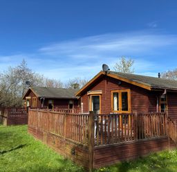 Two log cabins with wooden decks and satellite dishes at 2 Riverside Lodge Abercych near Cenarth