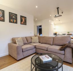 A living room with a beige corner sofa, a glass coffee table, three animal portraits on the wall at Hub House in Three Oaks near Hastings