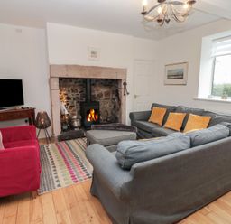 A living room with sofas around a fireplace and a television on a stand at The Smithy in Chathill near Seahouses