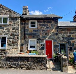 Stone cottages with white window frames and a red door with a small garden and a metal gate at Riverbank Cottage in Beddgelert
