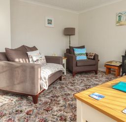 A living room with two brown armchairs a floral carpet a wooden table and wall decorations at Samson's Place in Morfa Bychan