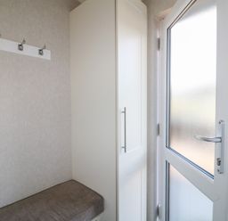 A small entryway with a bench, wall hooks, a tall white cabinet, and a frosted glass door at Stones Throw in Marston near Barkston