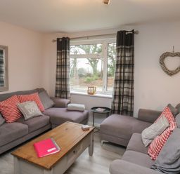A living room with two grey sofas, a wooden coffee table, a window with plaid curtains and a heart-shaped wall decoration at Lewis Lodge in St Ann's Chapel