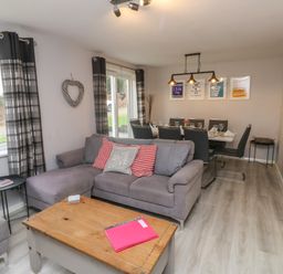 A living room with a gray sofa and coffee table next to a dining area with a table and chairs at Lewis Lodge in St Ann's Chapel