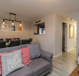 A living room with a gray sofa and pillows and a dining area with a table and chairs at Lewis Lodge in St Ann's Chapel