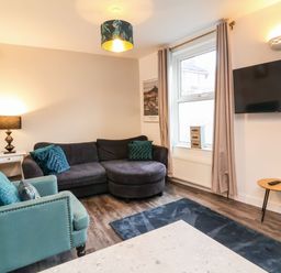 A living room with a dark grey corner sofa green armchair wall mounted tv and window with curtains at Hollycombe in Ilfracombe