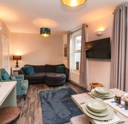 A living room with a sectional sofa an armchair a rug a wall-mounted tv and a dining table set for four at Hollycombe in Ilfracombe
