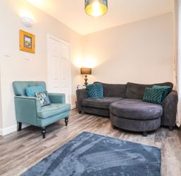 A living room with a gray sectional sofa blue armchair floor lamp blue rug and a window at Hollycombe in Ilfracombe