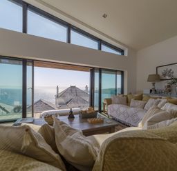 A living room with couches coffee table lamps and framed pictures with ocean view at Oystercatcher in Mevagissey
