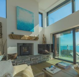 A living room with a wood stove TV and large windows overlooking the sea at Oystercatcher in Mevagissey