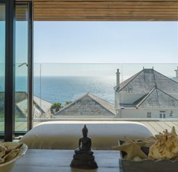 A room with a bed and decorative shells on a table with a sea view through glass doors at Oystercatcher in Mevagissey