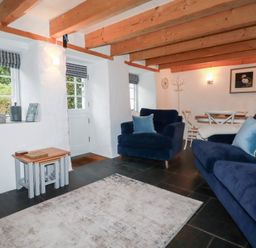 A living room with blue armchairs and sofa a wooden ceiling and a dining table at 2 Rose Cottage in St Agnes