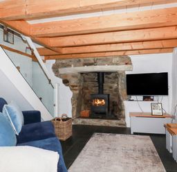 A living room with a blue sofa a stone fireplace with wood burner and a tv on a stand at 2 Rose Cottage in St Agnes
