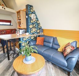 A living room with a blue sofa orange cushions floral wall clock and a wooden table at Sunflower Lodge Near Misterton