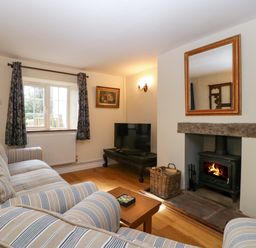 A living room with a striped sofa by a window a fireplace with a wood burning stove and a tv on a table at Court House Cottage in Gatcombe near Blakeney