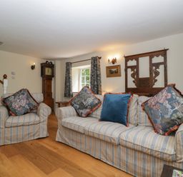 A living room with a sofa, armchair, and wall clock at Court House Cottage in Gatcombe near Blakeney