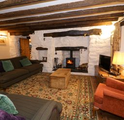 A living room with sofas and armchair around a fireplace with wooden beams on the ceiling at Glandwr Cottage in Llanbedr