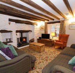 A living room with two sofas pillows a fireplace a wood stove an orange armchair a wooden chest and a television at Glandwr Cottage in Llanbedr