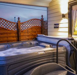 An outdoor hot tub with water jets active next to a wooden privacy fence and the entrance of a cabin at Binevanagh Cabin in Magilligan near Castlerock