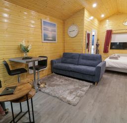 A wooden cabin interior with a sofa a bed a dining table with two chairs and a wall clock at Binevanagh Cabin in Magilligan near Castlerock