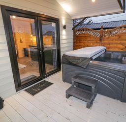 An outdoor deck area with a hot tub steps and glass double doors leading inside at MUSSENDEN CABIN Magilligan near Castlerock