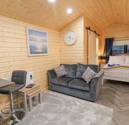 A wooden cabin interior with a sofa table and chair a bed with pillows and towels and a wall clock at MUSSENDEN CABIN Magilligan near Castlerock