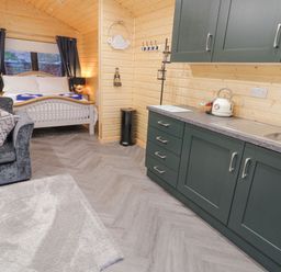 A kitchen area with dark green cabinets and a sink beside a sleeping area with a bed and black curtains at MUSSENDEN CABIN in Magilligan near Castlerock