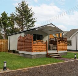 A small white cabin with a covered porch and wooden railings surrounded by grass at Benone Cabin in Magilligan near Castlerock