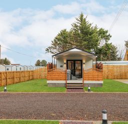 A small cabin with a porch and wooden fencing on a grass lawn at Benone Cabin in Magilligan near Castlerock