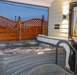 An outdoor hot tub with wooden lattice fencing and an open door to a room at Benone Cabin Magilligan near Castlerock