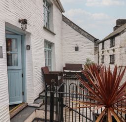 An outdoor patio area with chairs and a table beside white stone buildings at Teana Cottage in Polperro