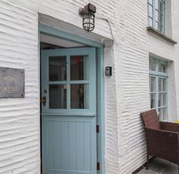 A blue door on a white textured wall with a sign reading Teana Cottage and wicker chairs outside at Teana Cottage in Polperro