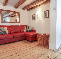 A living room with a red sectional sofa and nesting tables on a wooden floor at Teana Cottage in Polperro