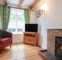 A living room with a red armchair green curtains a wooden TV stand with a TV and a fireplace at Teana Cottage in Polperro