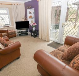 A living room with brown leather sofas a television on a stand and glass doors leading outside at Greenhaven in Narberth