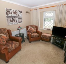 A living room with two armchairs a footstool a television on a stand a side table with a lamp and flowers on a side table at Greenhaven in Narberth