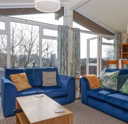 A living room with blue sofas wooden coffee table and dining area at Matilda Lodge in Newton Ferrers