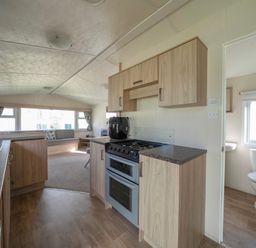 A kitchen with wooden cabinets and appliances next to a bathroom with a toilet and window at Ripples & Reeds - Billing Aquadrome in Billing Aquadrome Holiday Park