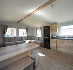 A kitchen and living area with wooden cabinets a black refrigerator a gray couch and a wooden dining table at Kingfisher Caravan - Billing Aquadrome in Billing Aquadrome Holiday Park