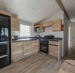 A kitchen with wooden cabinets a black refrigerator a toaster a kettle a stove and an oven at Kingfisher Caravan - Billing Aquadrome Holiday Park