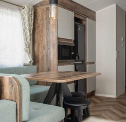 A kitchen and dining area with a wooden table black stools a built-in microwave and refrigerator at Stillwater Retreat - Billing Aquadrome Holiday Park