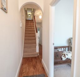 A hallway with wooden flooring leading to carpeted stairs and a partially visible room with a wooden bench and a fur throw at 34 North Denes Road in Great Yarmouth