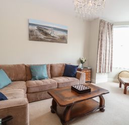 A living room with a beige sofa and blue cushions a wooden coffee table and a side table with flowers at 34 North Denes Road in Great Yarmouth