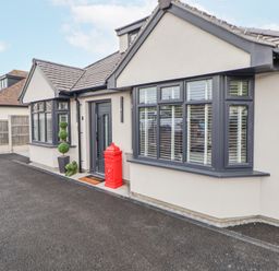 Exterior view of a single-story house with grey window frames a red post box near the black front door and potted plants at Ty Blodau near Prestatyn