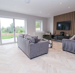A living room with two gray sofas a green armchair a television mounted on a wooden panel and large glass doors at Ty Blodau near Prestatyn