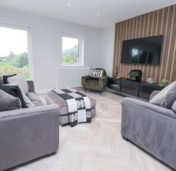 A living room with two sofas a chair ottoman and a wall-mounted television at Ty Blodau near Prestatyn