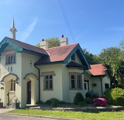 A cream colored house with a red roof and green trim surrounded by plants and trees at Hafod Lodge in Hensol near Pontyclun