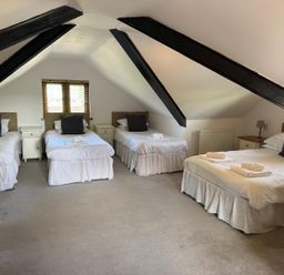 A bedroom with four beds under a sloped ceiling with black beams at Hafod Lodge in Hensol near Pontyclun