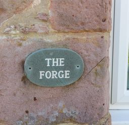 A green oval plaque with the words The Forge on a stone wall next to a white window at The Forge in Nr Seashouses